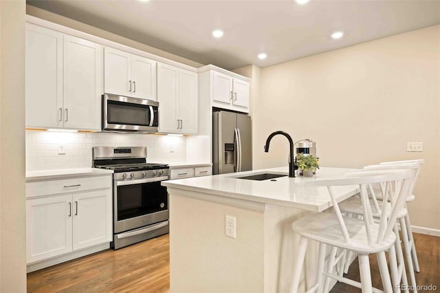 kitchen featuring a breakfast bar, a sink, light wood-style floors, a center island with sink, and appliances with stainless steel finishes