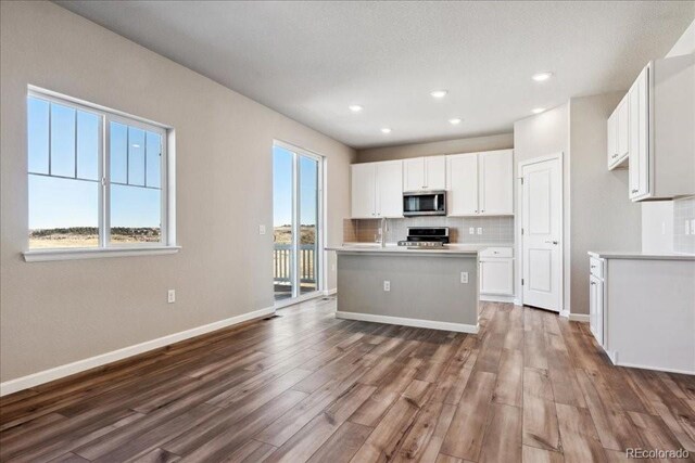 kitchen featuring white cabinetry, stainless steel appliances, backsplash, a kitchen island with sink, and wood-type flooring