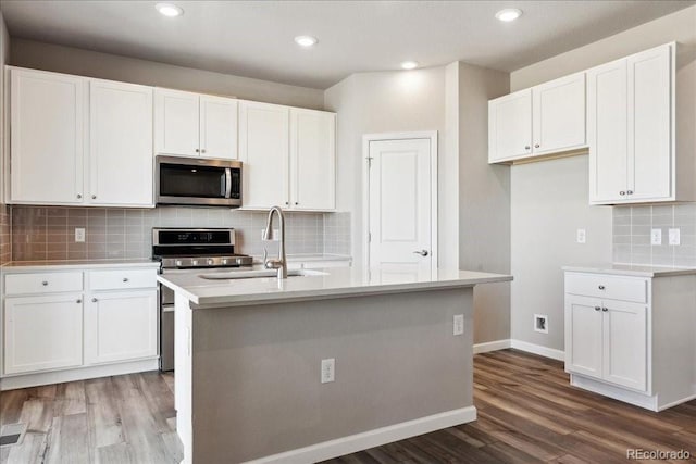 kitchen with hardwood / wood-style flooring, appliances with stainless steel finishes, white cabinets, and a kitchen island with sink