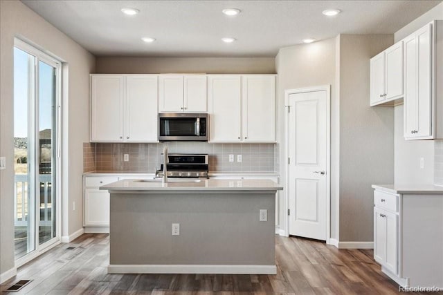 kitchen featuring white cabinetry, appliances with stainless steel finishes, a center island with sink, and hardwood / wood-style floors