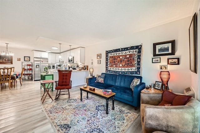 living room with light wood finished floors, a textured ceiling, and an inviting chandelier