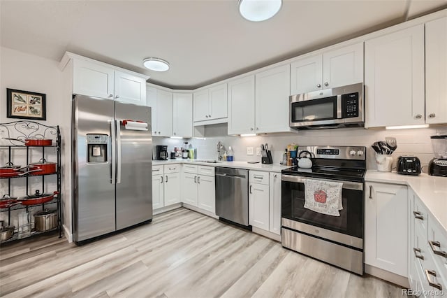 kitchen with stainless steel appliances, light countertops, light wood-style flooring, and tasteful backsplash