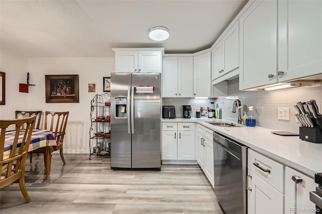 kitchen featuring a sink, white cabinetry, appliances with stainless steel finishes, backsplash, and light wood finished floors