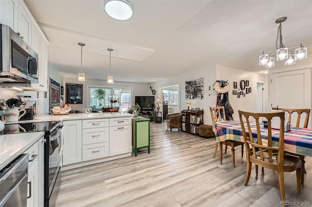 kitchen featuring light wood-style flooring, stainless steel appliances, a peninsula, open floor plan, and light countertops