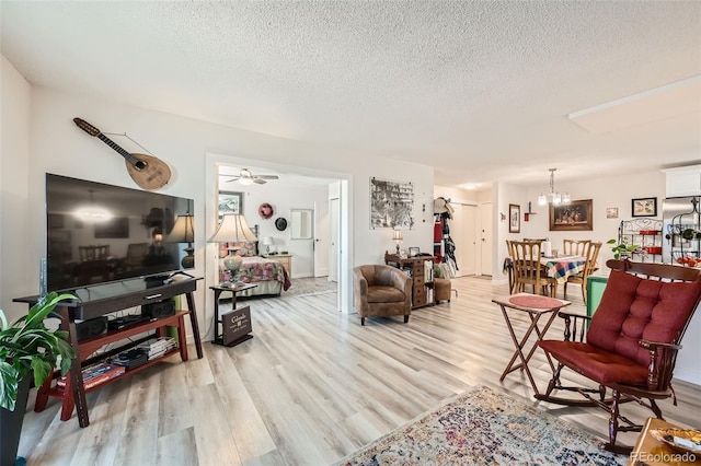 living room with light wood finished floors, a textured ceiling, and ceiling fan with notable chandelier