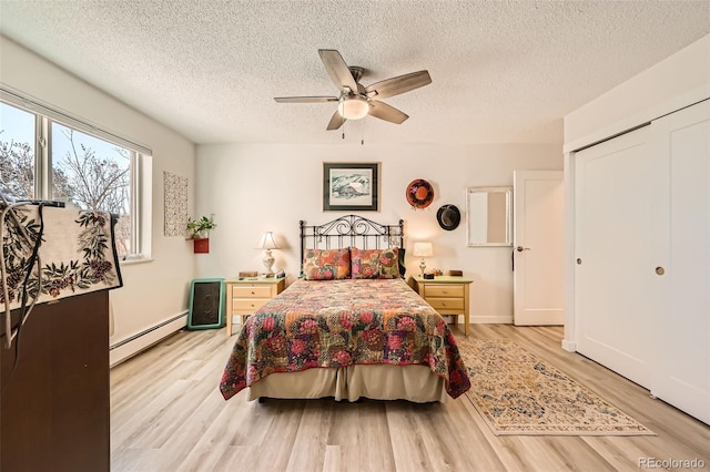 bedroom featuring ceiling fan, baseboard heating, a textured ceiling, and light wood-style flooring