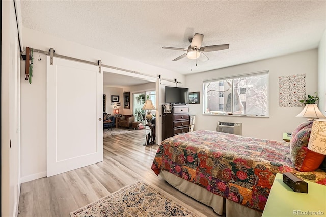 bedroom with a wall mounted AC, a barn door, ceiling fan, a textured ceiling, and wood finished floors