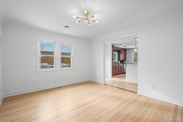 spare room featuring sink, light hardwood / wood-style flooring, a wealth of natural light, and a chandelier