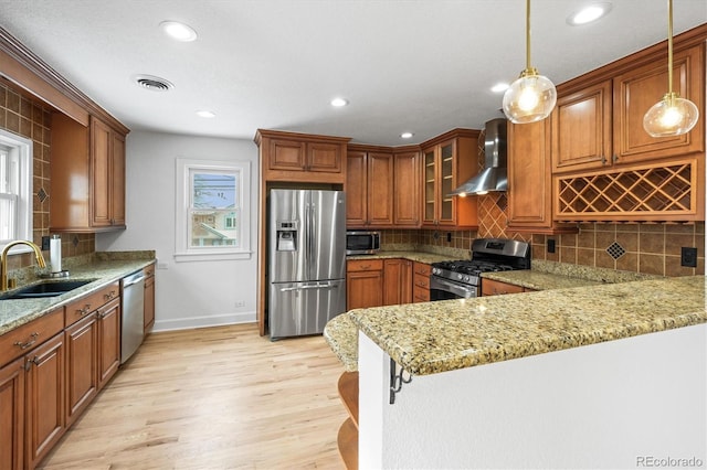 kitchen featuring pendant lighting, sink, wall chimney exhaust hood, appliances with stainless steel finishes, and kitchen peninsula