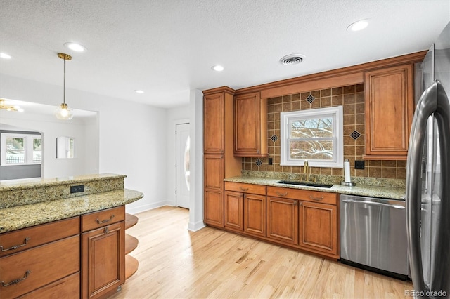 kitchen with sink, light stone counters, backsplash, pendant lighting, and appliances with stainless steel finishes