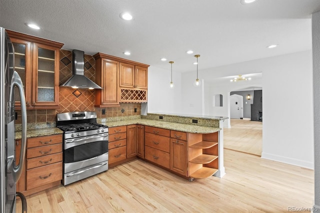 kitchen featuring wall chimney range hood, hanging light fixtures, light hardwood / wood-style floors, kitchen peninsula, and stainless steel appliances