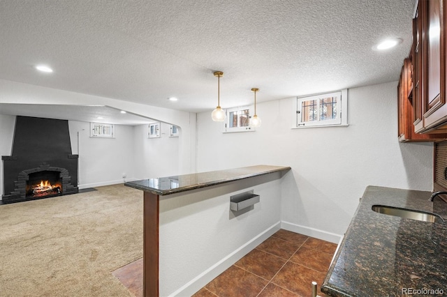 kitchen with sink, a brick fireplace, kitchen peninsula, dark stone countertops, and decorative light fixtures