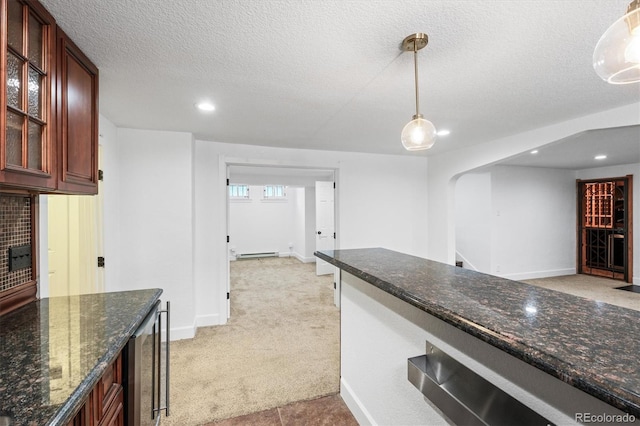 kitchen with a textured ceiling, light colored carpet, baseboard heating, dark stone countertops, and hanging light fixtures