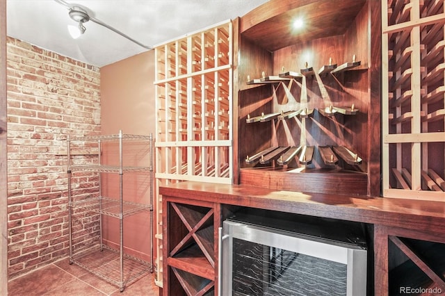 wine room with bar area, tile patterned floors, wine cooler, and brick wall