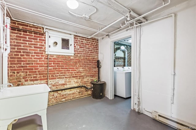 basement featuring brick wall, sink, a baseboard heating unit, and washing machine and clothes dryer