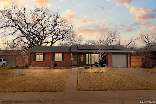 view of front facade with roof mounted solar panels, brick siding, driveway, and an attached garage