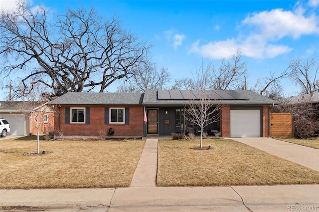 view of front of property with brick siding, solar panels, concrete driveway, an attached garage, and a front lawn