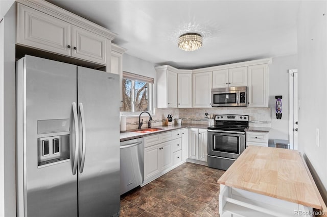 kitchen featuring a chandelier, stainless steel appliances, a sink, white cabinets, and decorative backsplash