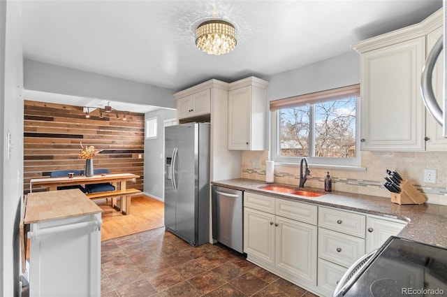 kitchen featuring tasteful backsplash, an inviting chandelier, stainless steel appliances, wood walls, and a sink