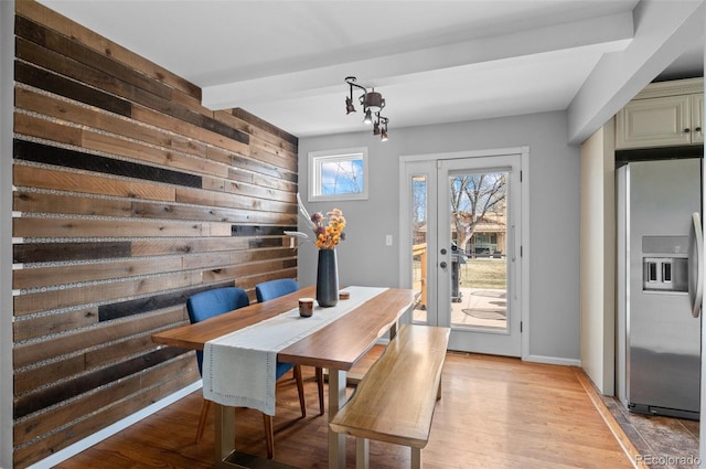 dining area featuring wood walls, light wood-type flooring, beam ceiling, and baseboards