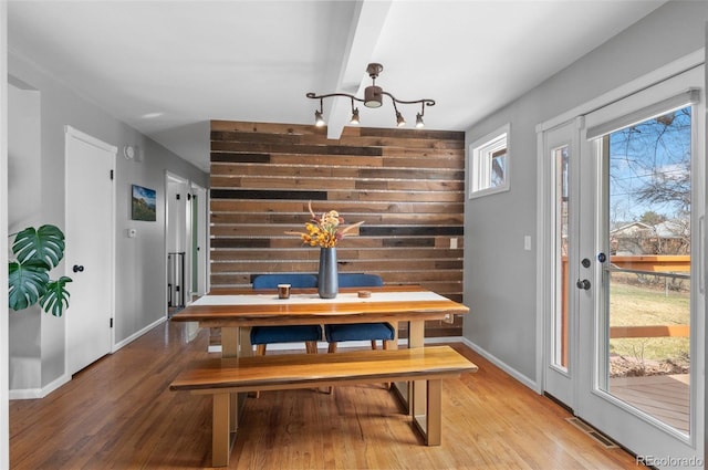 dining room featuring an accent wall, wood walls, visible vents, baseboards, and light wood finished floors