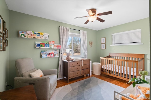 bedroom with a nursery area, ceiling fan, and wood finished floors