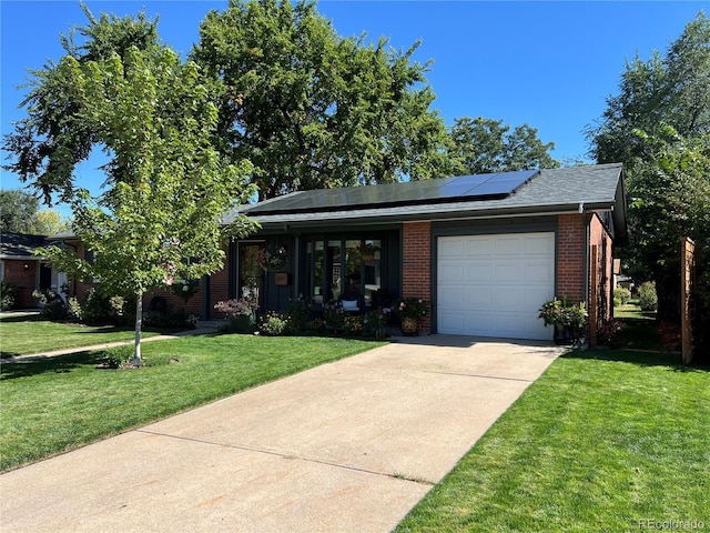 view of front of house with brick siding, solar panels, a front yard, a garage, and driveway