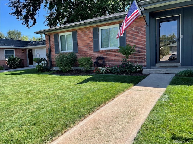 view of front of home featuring an attached garage, brick siding, and a front yard