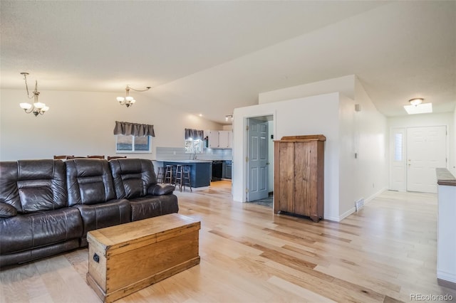 living room featuring sink, light wood-type flooring, lofted ceiling, and an inviting chandelier