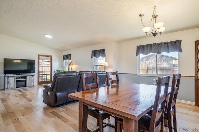 dining room featuring a textured ceiling, an inviting chandelier, light hardwood / wood-style flooring, and lofted ceiling