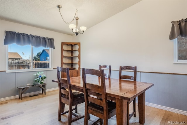 dining space featuring wood walls, a notable chandelier, light hardwood / wood-style floors, and a textured ceiling