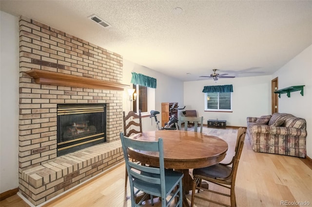 dining area with ceiling fan, light hardwood / wood-style floors, a textured ceiling, and a brick fireplace