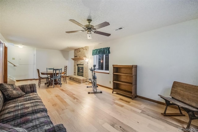 interior space with ceiling fan, a fireplace, light hardwood / wood-style floors, and a textured ceiling