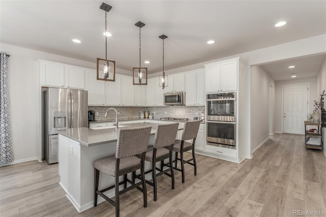 12513 Shore Point St, Firestone, CO 80504 - kitchen with stainless steel appliances, a sink, light wood-style floors, decorative backsplash, and a center island with sink