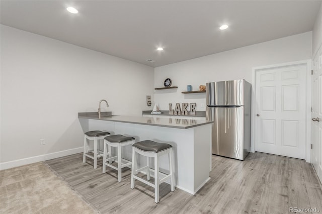 12513 Shore Point St, Firestone, CO 80504 - kitchen with freestanding refrigerator, a breakfast bar, light wood-type flooring, a peninsula, and open shelves