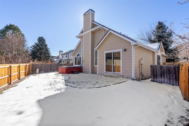 snow covered back of property with a hot tub