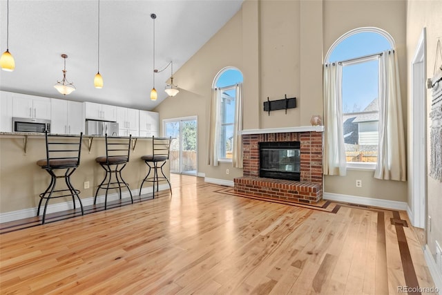 living room featuring high vaulted ceiling, a fireplace, and light hardwood / wood-style floors