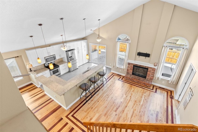 living room featuring a textured ceiling, a brick fireplace, high vaulted ceiling, light wood-type flooring, and sink