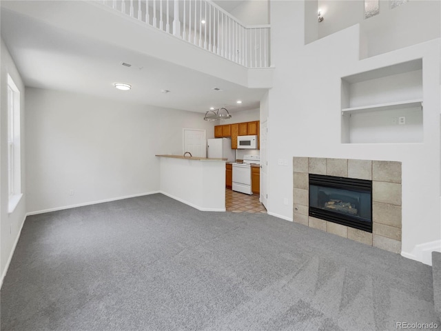 unfurnished living room with a tile fireplace, a towering ceiling, and light colored carpet