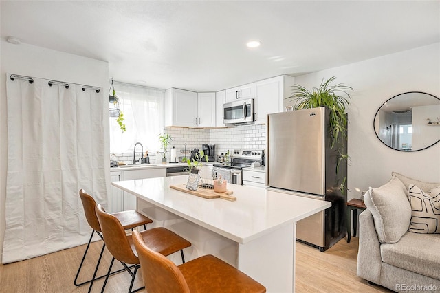 kitchen featuring white cabinets, appliances with stainless steel finishes, a kitchen bar, and light wood-style floors