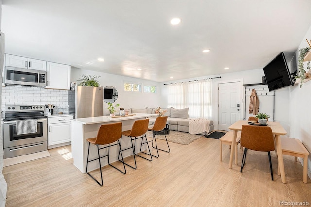 kitchen with stainless steel appliances, a kitchen breakfast bar, light wood-style floors, and white cabinets