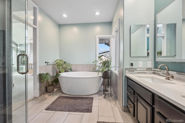full bath featuring vanity, a soaking tub, a wainscoted wall, recessed lighting, and a stall shower