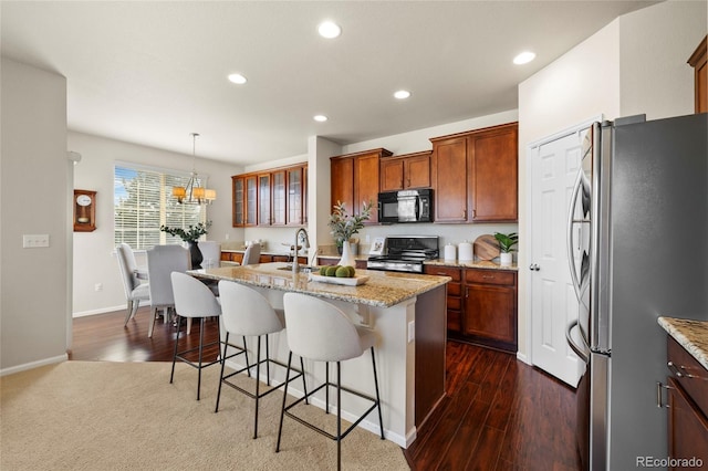 kitchen featuring light stone counters, a breakfast bar area, stainless steel appliances, recessed lighting, and an island with sink