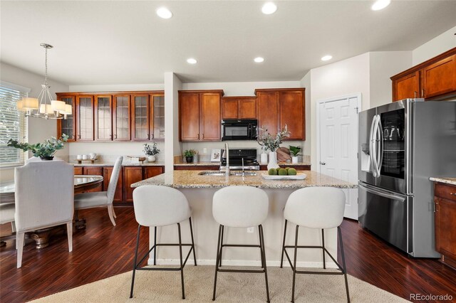 kitchen with black microwave, recessed lighting, a sink, stainless steel fridge, and a center island with sink