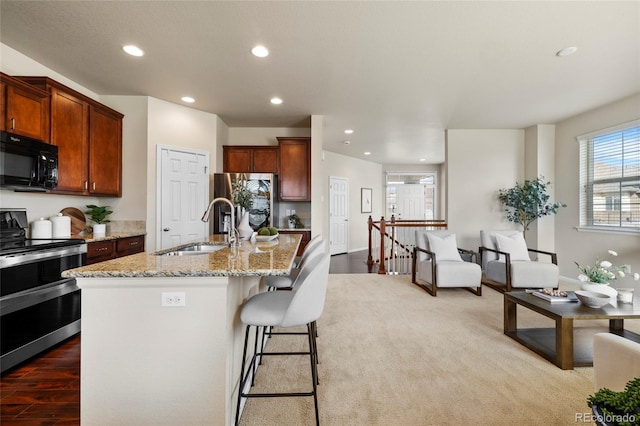 kitchen featuring a breakfast bar, light stone countertops, stainless steel appliances, a sink, and recessed lighting