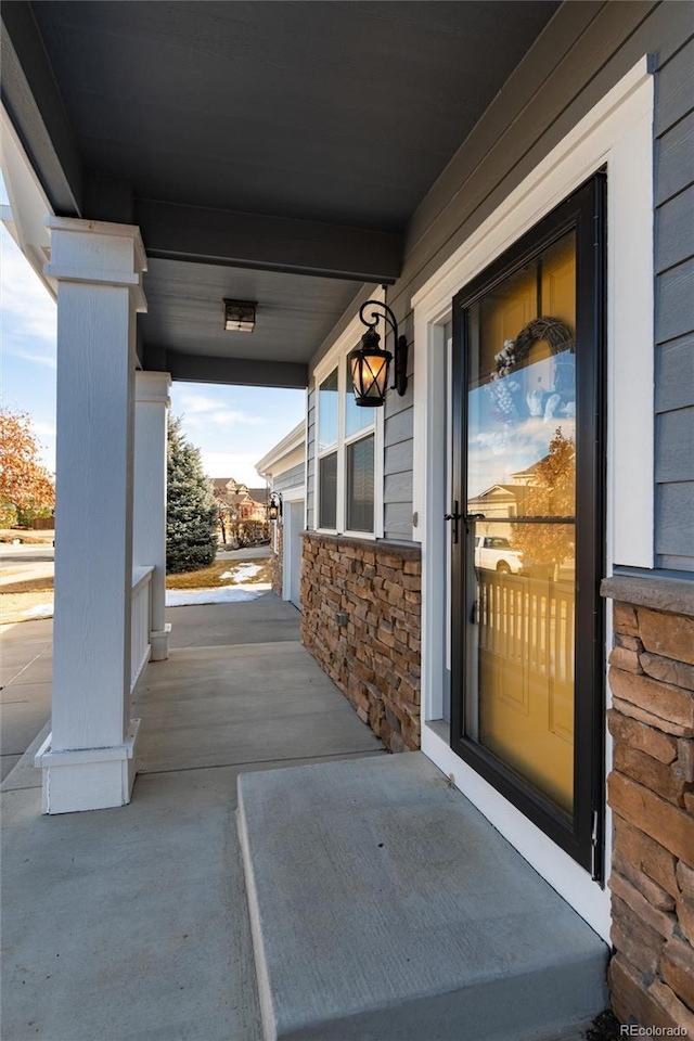 view of exterior entry featuring stone siding and covered porch