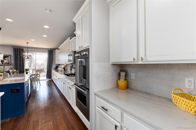 kitchen featuring stainless steel appliances, a sink, white cabinetry, blue cabinetry, and dark wood finished floors