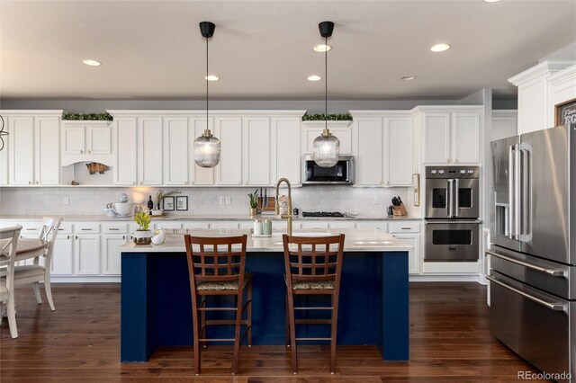 kitchen featuring a kitchen island with sink, dark wood-type flooring, light countertops, appliances with stainless steel finishes, and pendant lighting