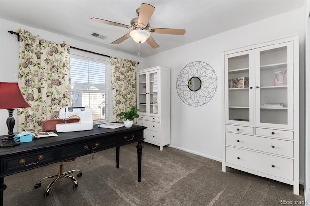 home office with a ceiling fan, dark colored carpet, visible vents, and baseboards