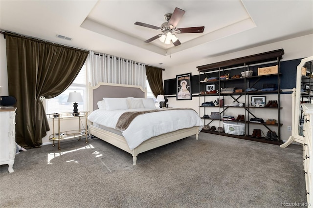 carpeted bedroom with visible vents, a tray ceiling, and a ceiling fan